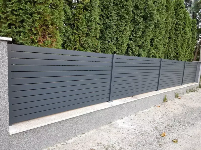 Antracit alumínium léckerítés tuják mellett, beton lábazaton